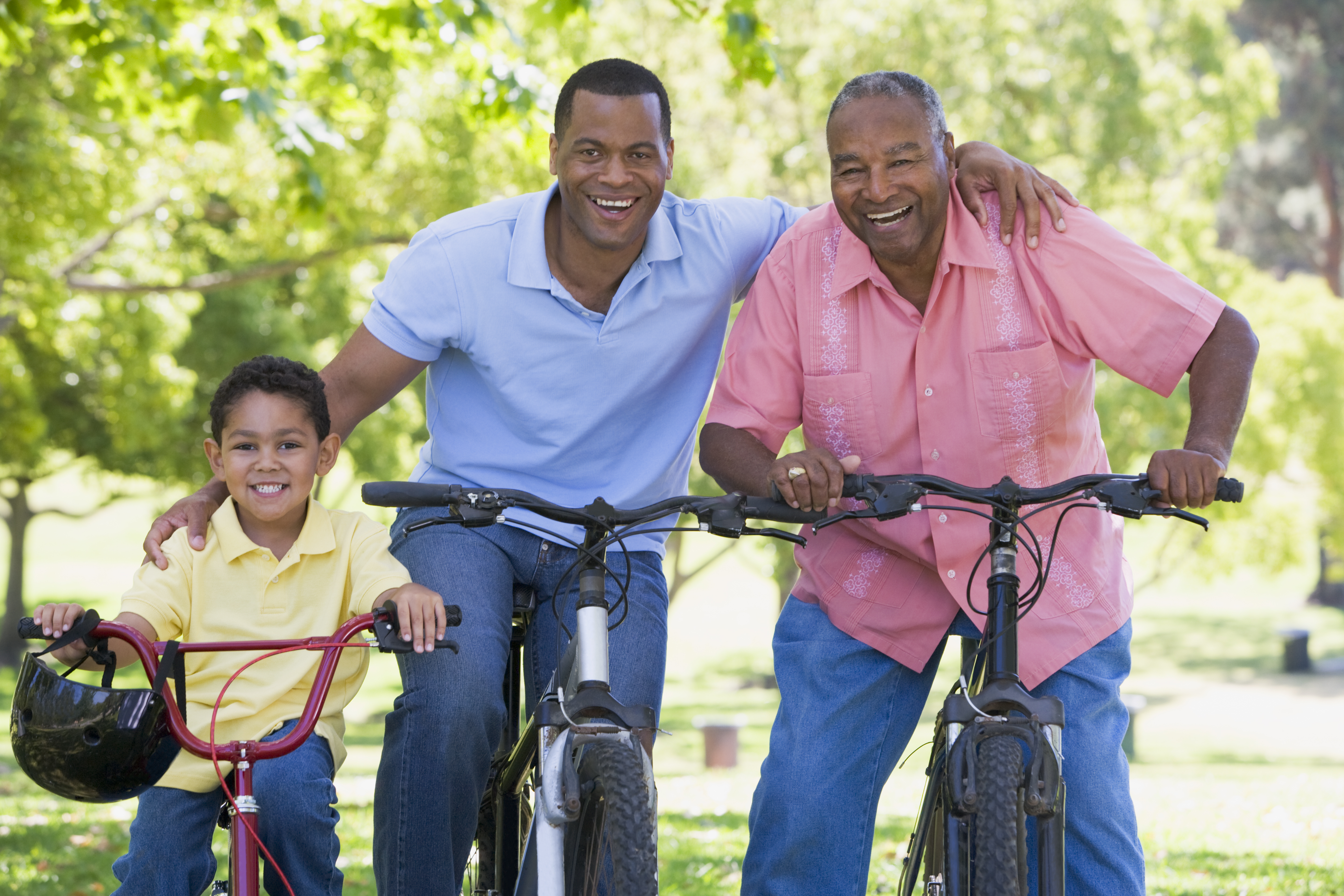 3 generations of males smiling and enjoying a bike ride together posing for the camera.